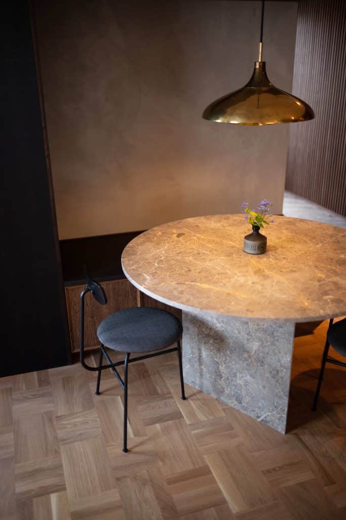 Rum med vägg i ljusgrå microcement som matchar inredningen av bord, stolar och lampor i förgrunden.